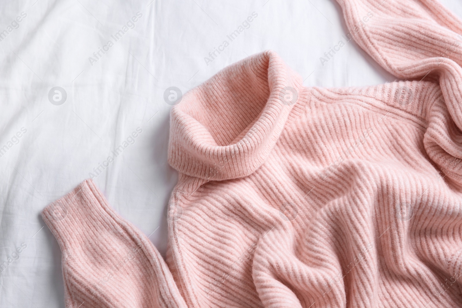 Photo of Pink warm sweater on white crumpled fabric, top view