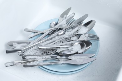 Washing silver spoons, forks and knives in foam