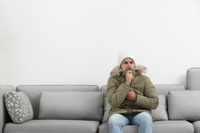 Photo of Young man in warm clothes freezing on sofa against white background