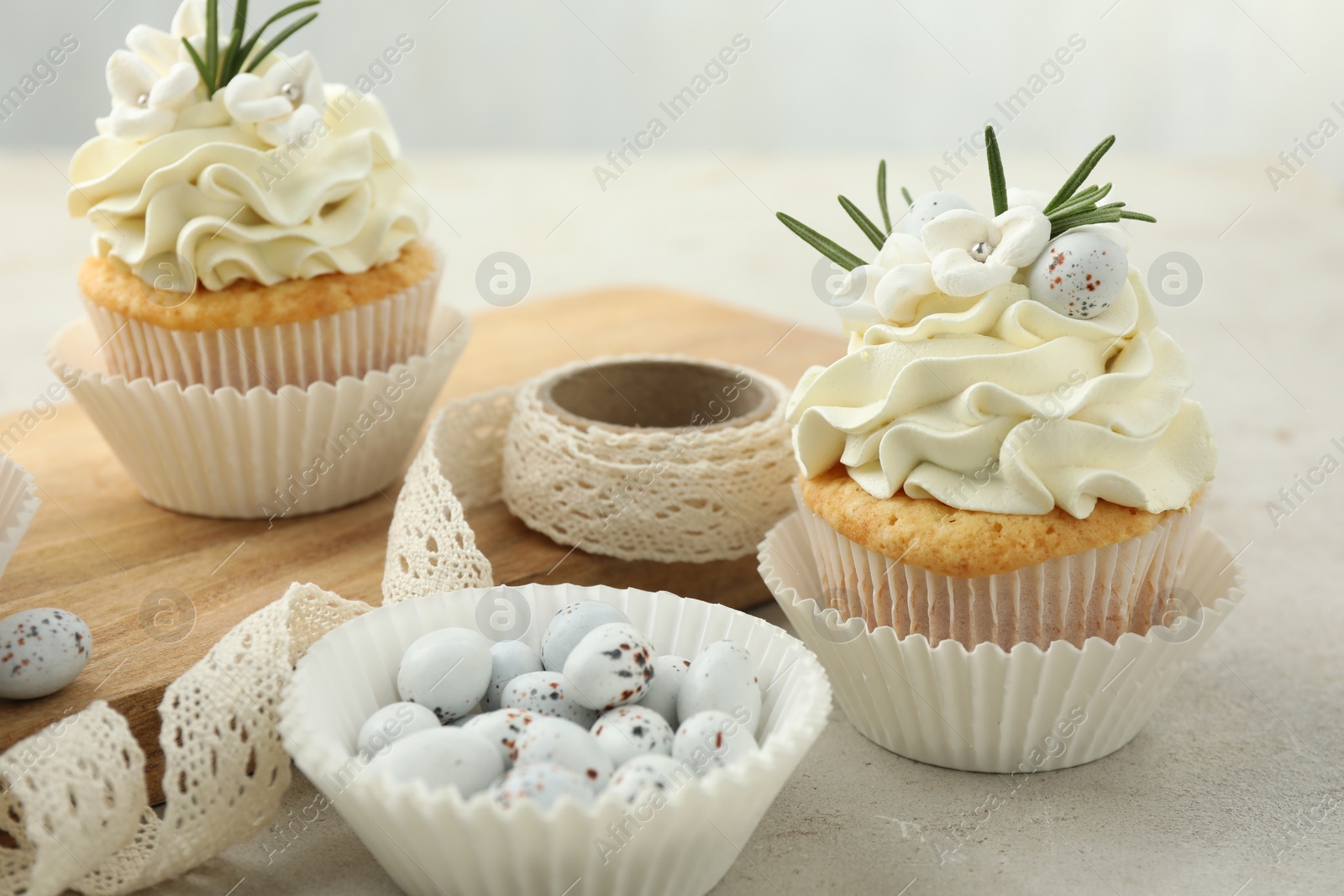 Photo of Tasty Easter cupcakes with vanilla cream, candies and ribbon on gray table, closeup