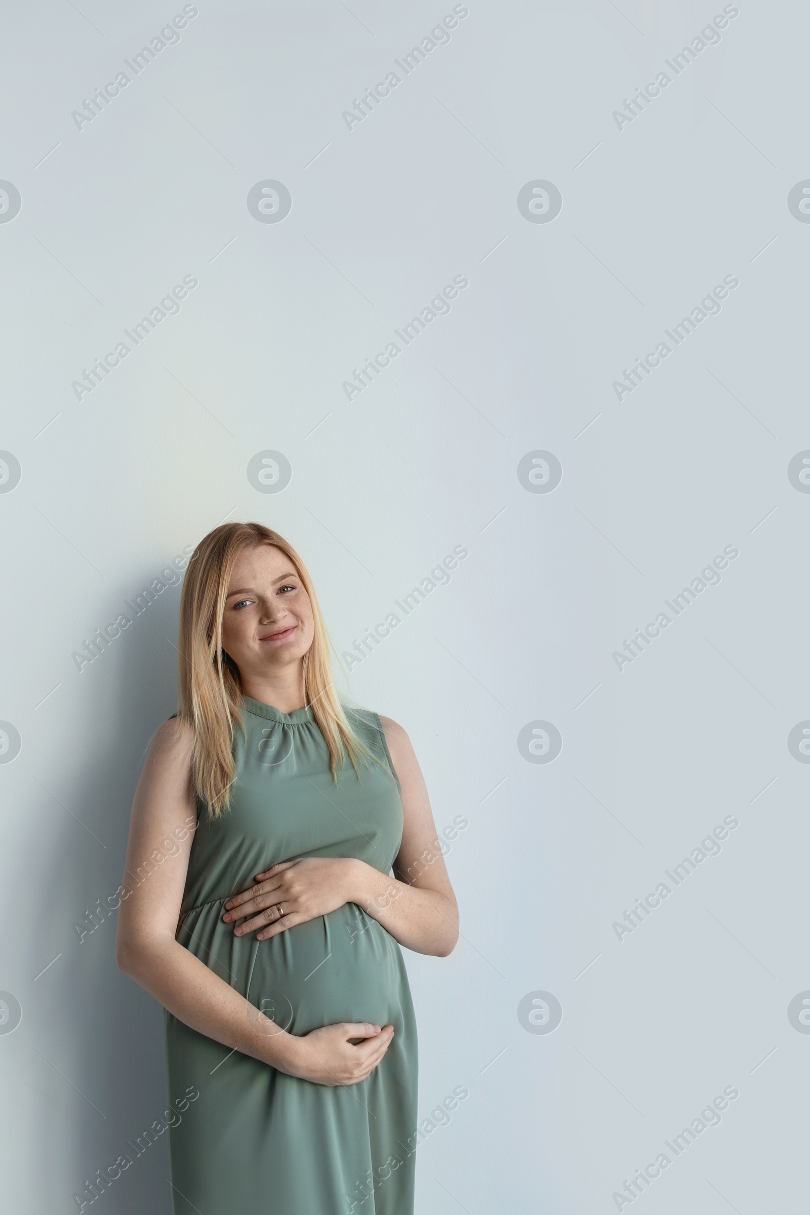 Photo of Young pregnant woman touching belly on light background