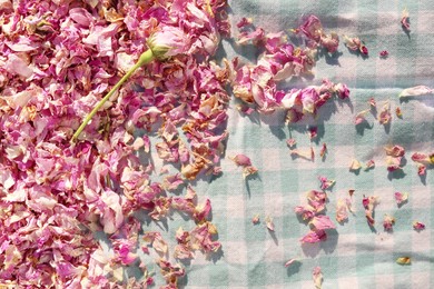 Photo of Scattered dried tea rose flowers and petals on checkered fabric, top view