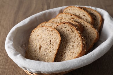 Photo of Fresh bread slices in wicker basket on wooden table, closeup