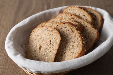 Fresh bread slices in wicker basket on wooden table, closeup