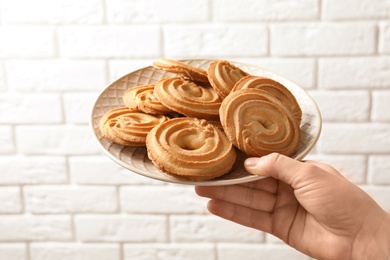 Woman holding plate with Danish butter cookies against white brick wall, closeup