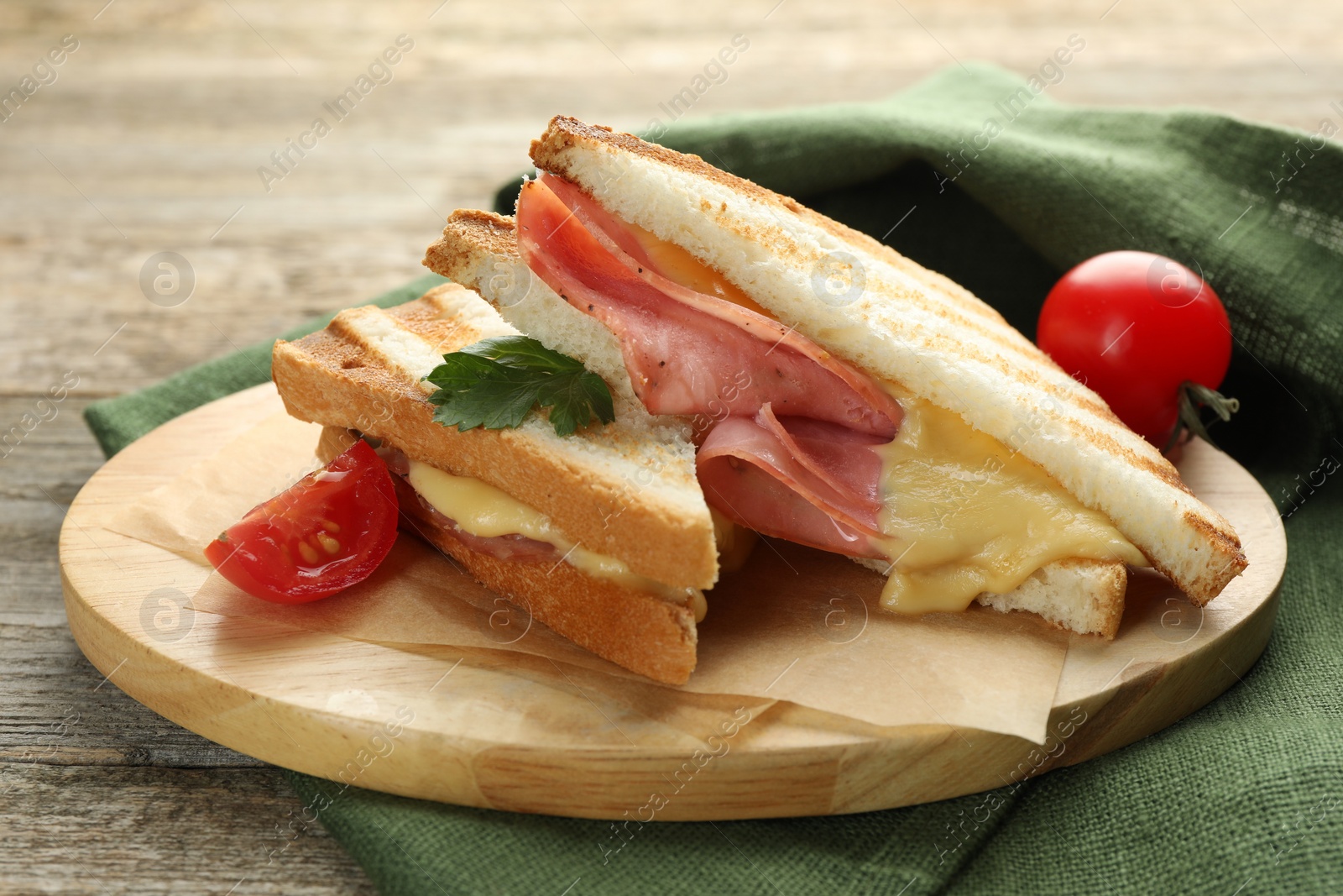 Photo of Tasty sandwiches with ham, parsley, melted cheese and tomato on wooden table, closeup