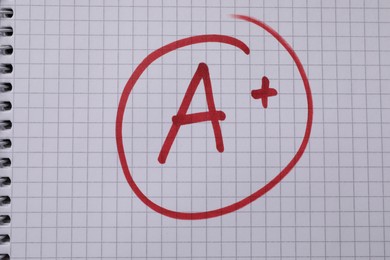 Photo of School grade. Red letter A with plus symbol on notebook paper, top view