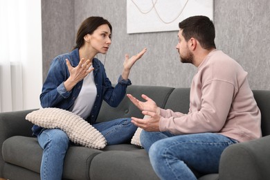 Photo of Emotional couple arguing on sofa indoors. Relationship problems