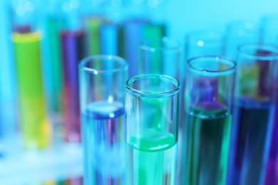 Many test tubes with colorful liquids on light blue background, closeup