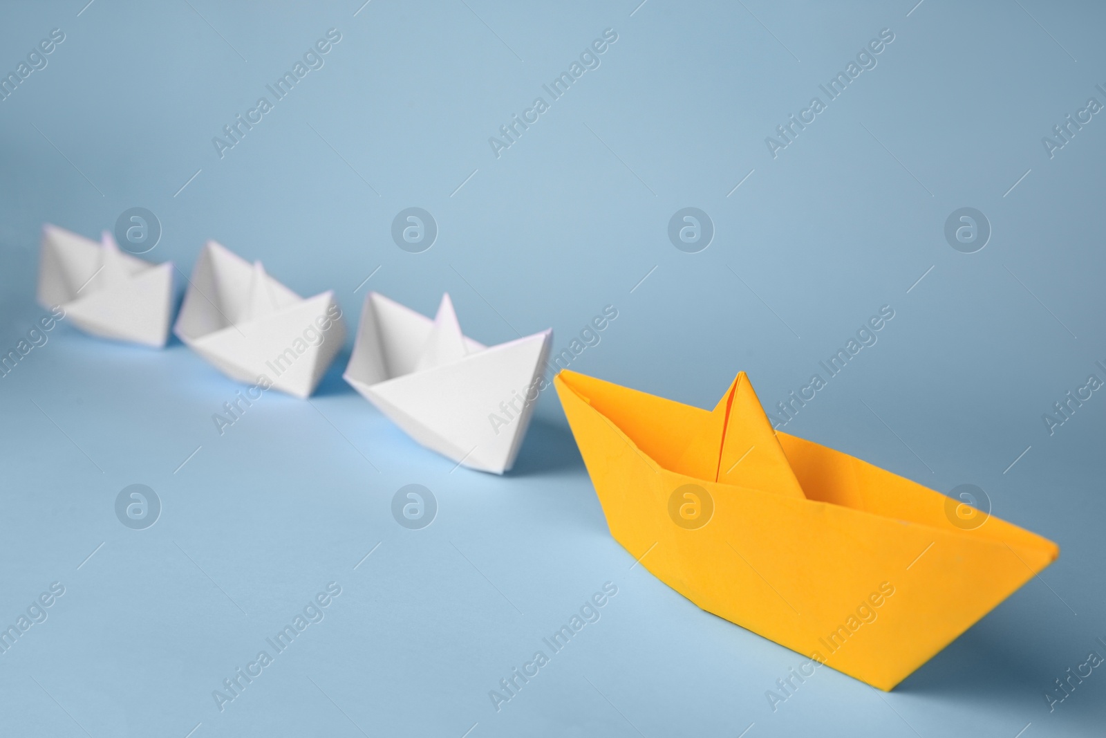 Photo of Group of paper boats following yellow one on light blue background. Leadership concept