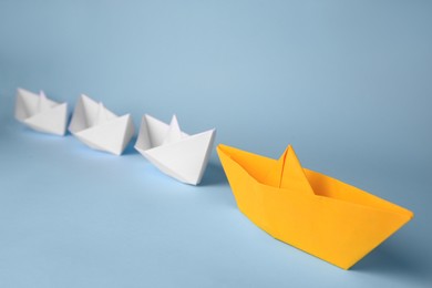 Group of paper boats following yellow one on light blue background. Leadership concept