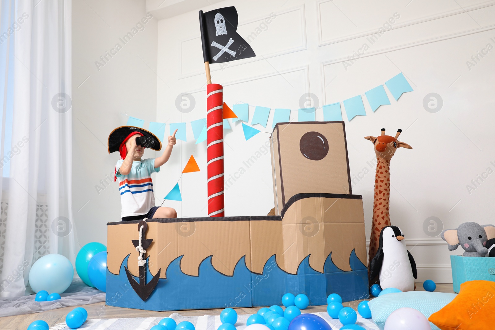 Photo of Little boy playing with binoculars in pirate cardboard ship at home. Child's room interior