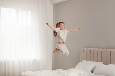 Photo of Cute little girl jumping on bed at home