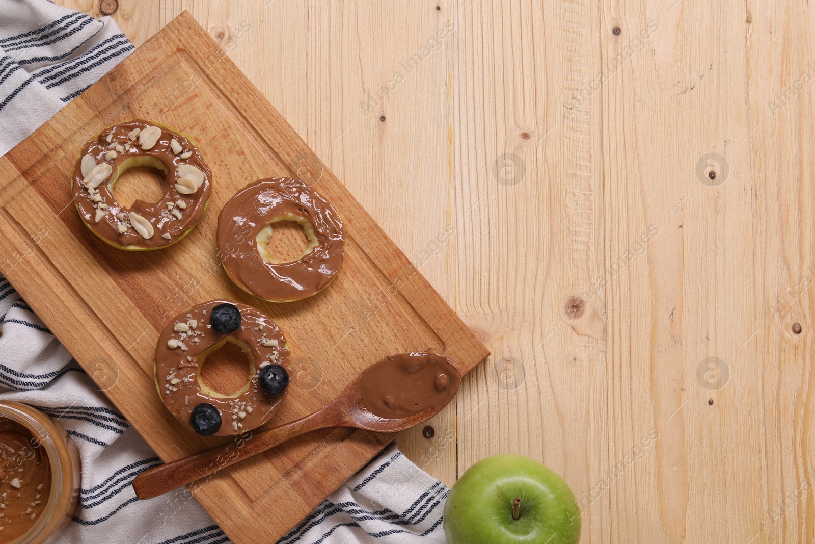 Photo of Slices of fresh apple with nut butter, blueberries and peanuts on wooden table, flat lay. Space for text