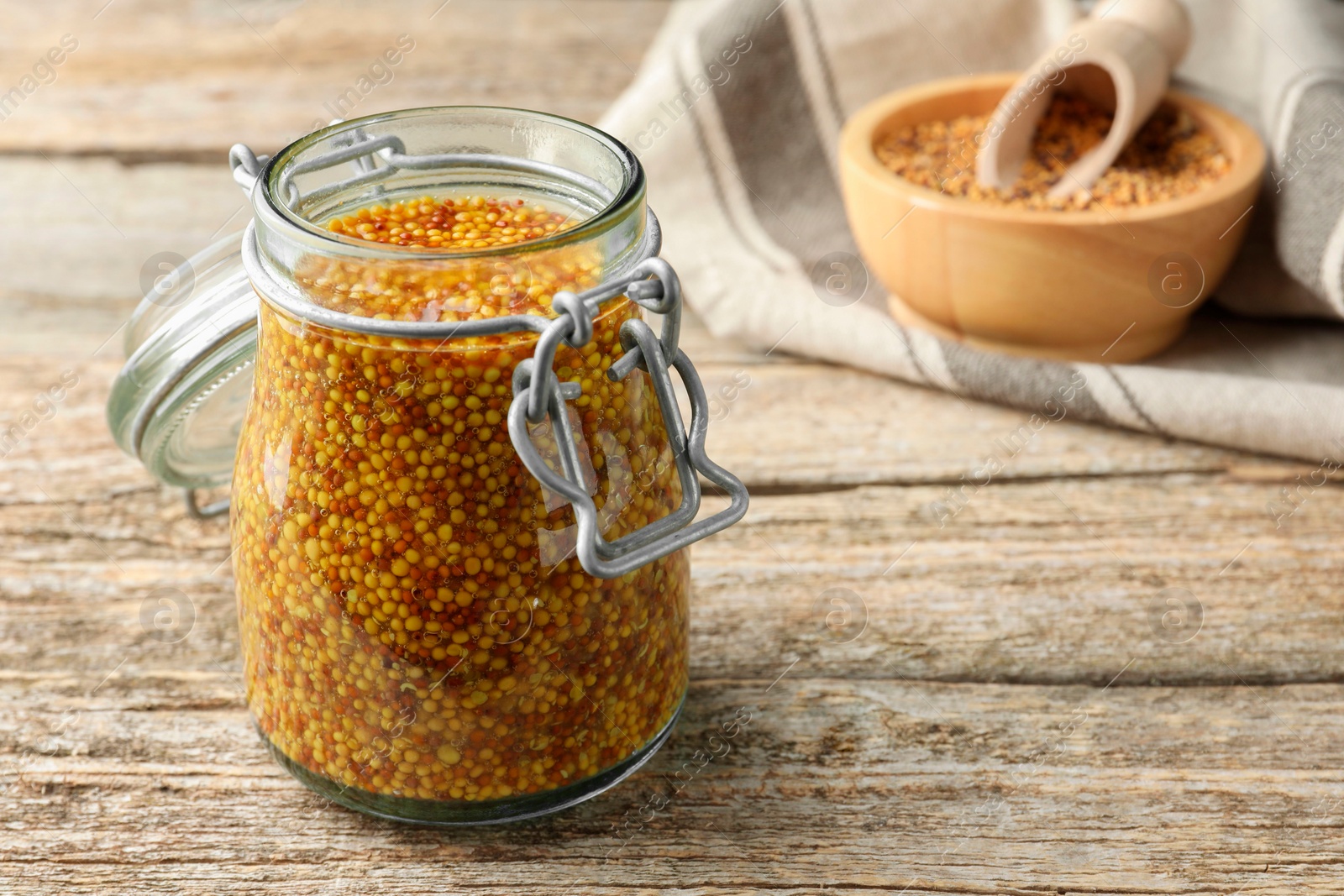 Photo of Whole grain mustard in jar on wooden table. Space for text