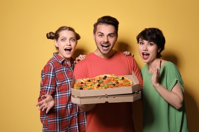 Group of friends with delicious pizza on color background