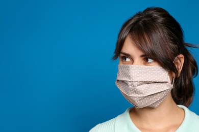 Young woman in protective face mask on blue background, space for text