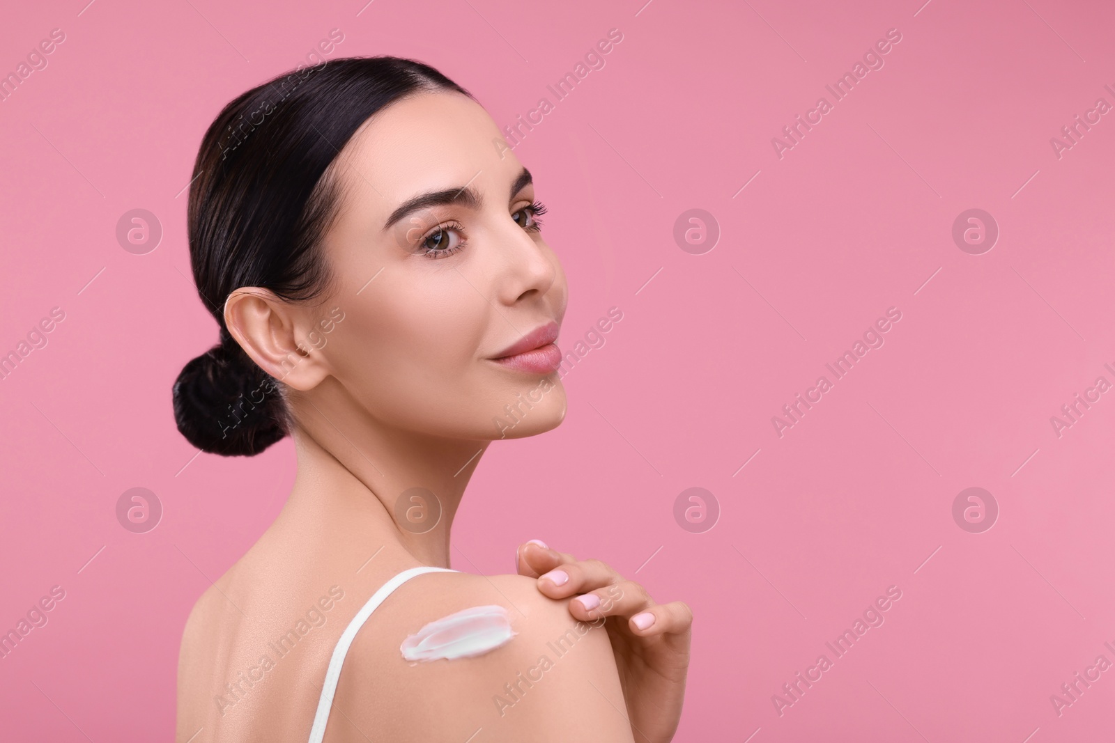 Photo of Beautiful woman with smear of body cream on her shoulder against pink background, space for text