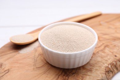 Bowl and spoon with active dry yeast on white table, closeup