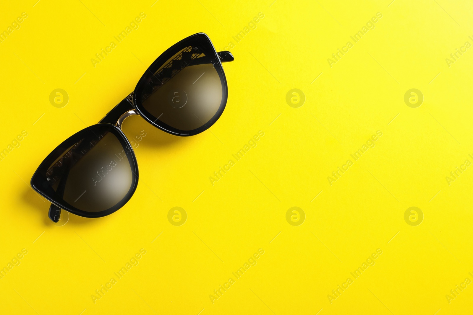 Photo of Stylish sunglasses on yellow background, top view. Space for text