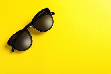 Stylish sunglasses on yellow background, top view. Space for text