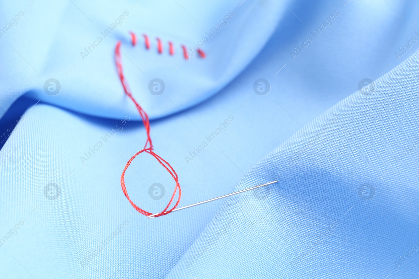 Photo of Sewing needle with thread and stitches on light blue cloth, selective focus