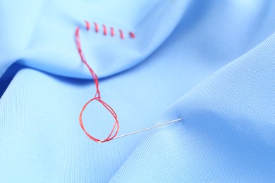 Photo of Sewing needle with thread and stitches on light blue cloth, selective focus