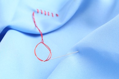 Sewing needle with thread and stitches on light blue cloth, selective focus