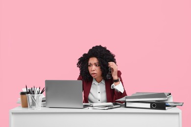 Stressful deadline. Scared woman looking at laptop at white desk on pink background
