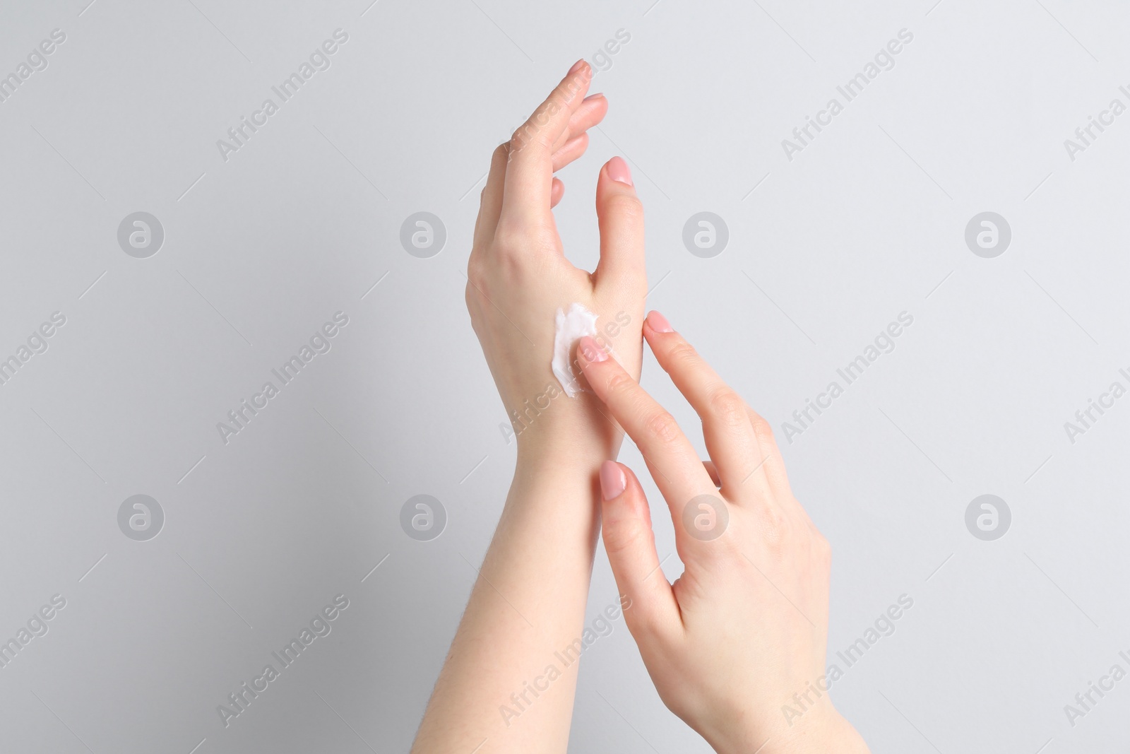 Photo of Woman applying cream on her hand against grey background, closeup