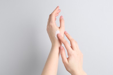 Woman applying cream on her hand against grey background, closeup