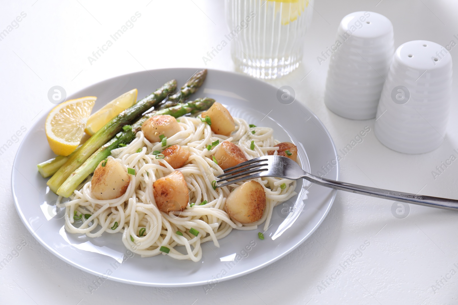 Photo of Delicious scallop pasta with asparagus, green onion and lemon served on white table, closeup