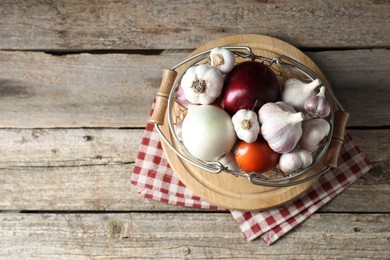 Fresh raw garlic and onions in metal basket on wooden table, top view. Space for text