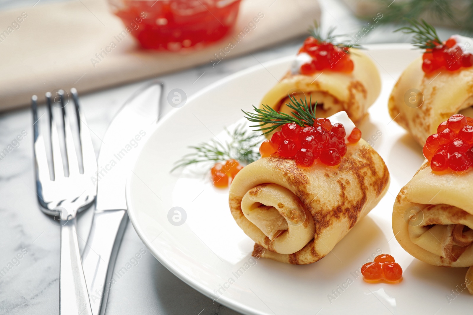 Photo of Delicious thin pancakes with red caviar on white marble table, closeup