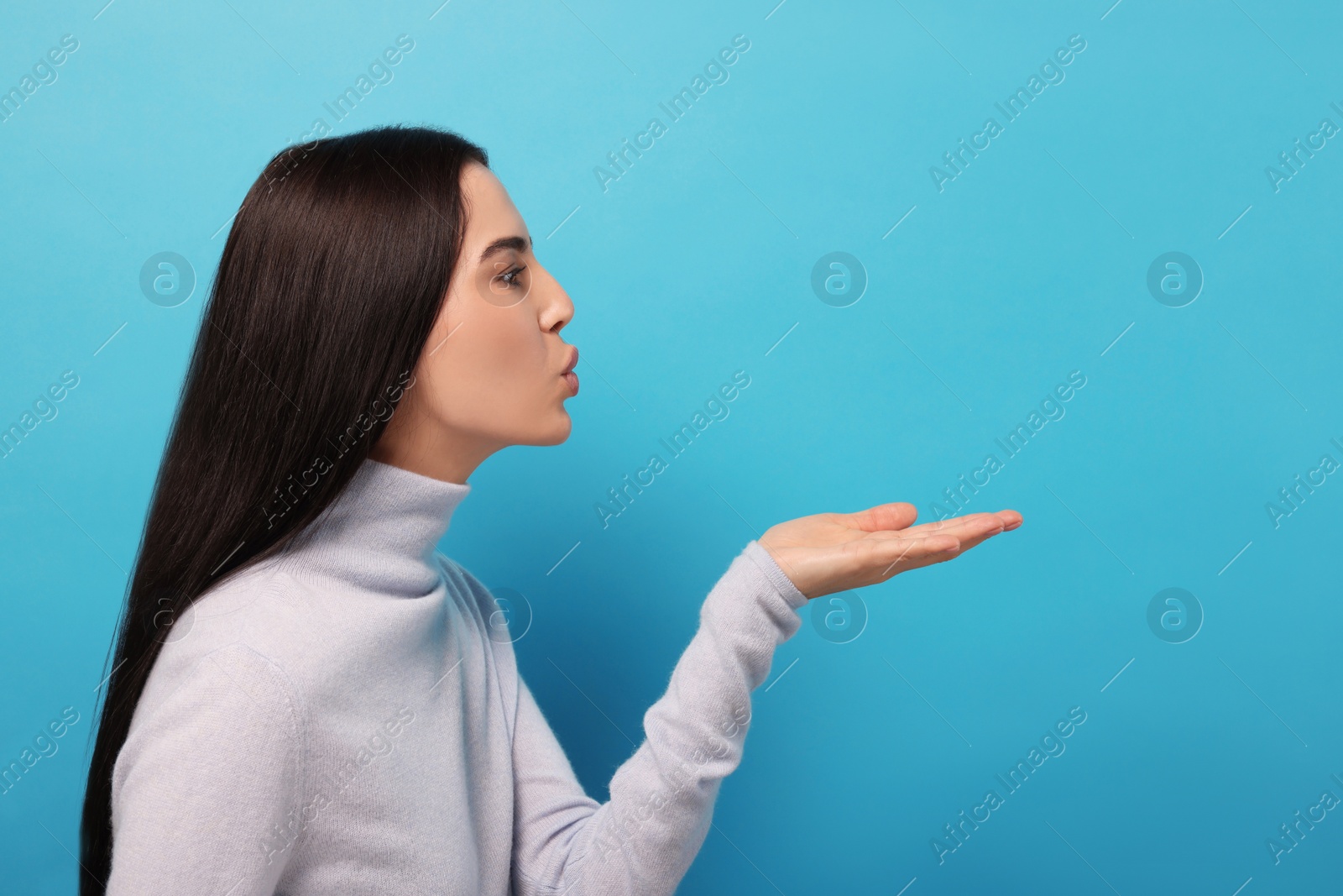 Photo of Beautiful young woman blowing kiss on light blue background. Space for text