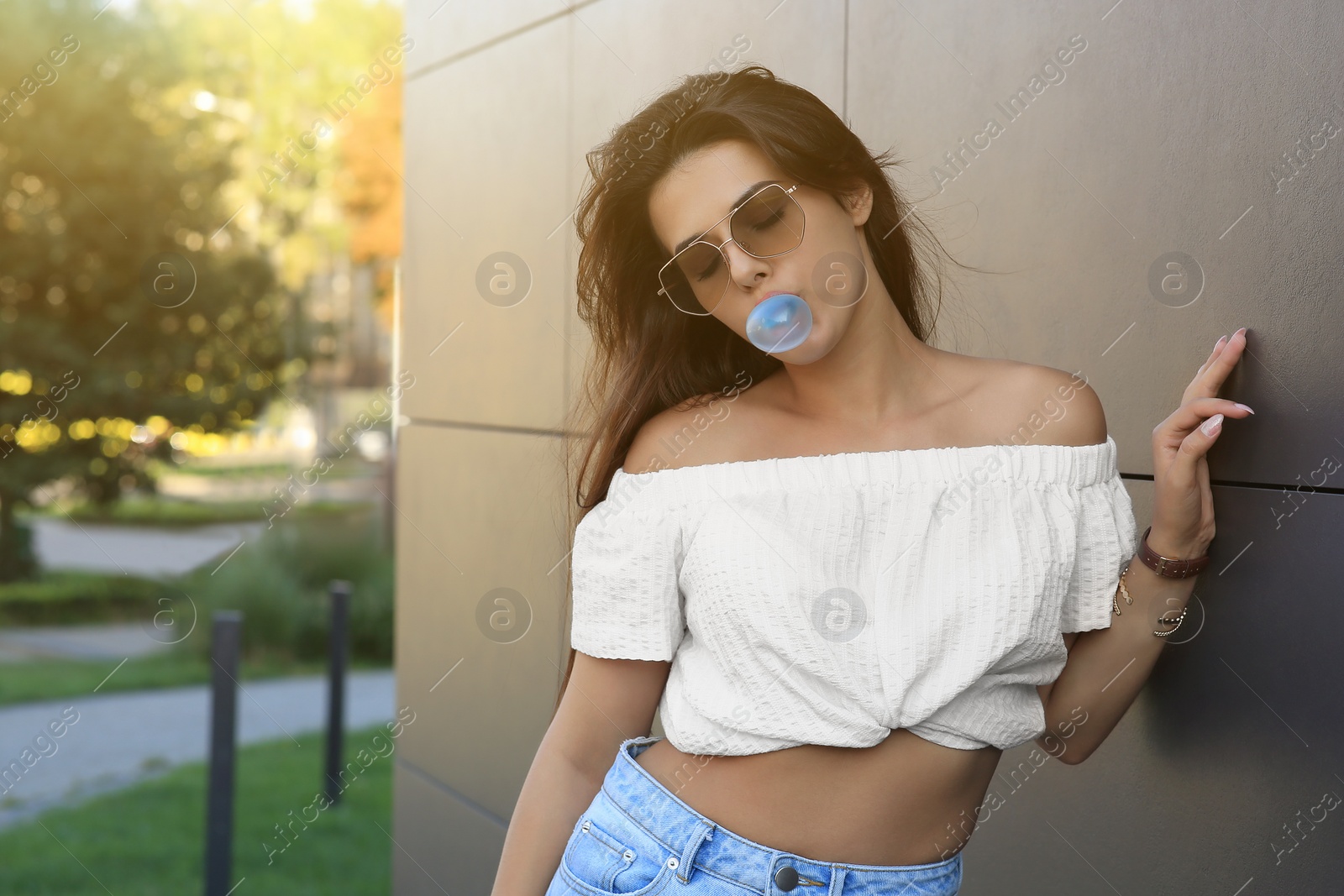 Photo of Beautiful woman blowing gum near dark tiled wall outdoors, space for text
