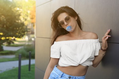 Beautiful woman blowing gum near dark tiled wall outdoors, space for text