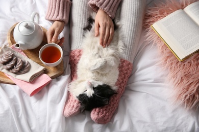 Photo of Woman stroking adorable cat on bed, top view