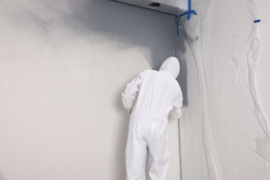 Photo of Decorator painting wall with spray, back view