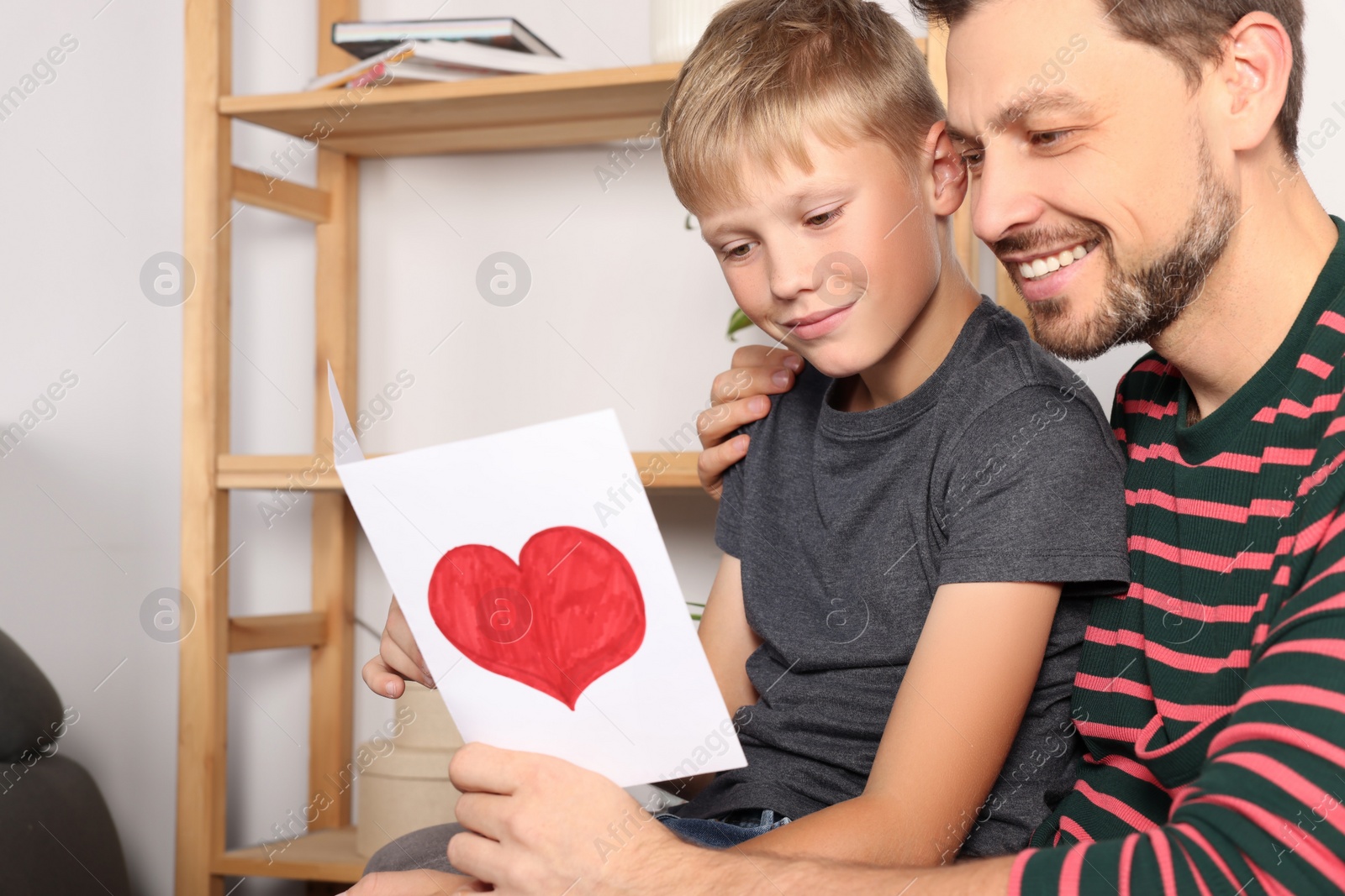 Photo of Happy man receiving greeting card from his son at home