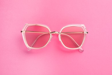 Photo of New stylish sunglasses on pink background, top view