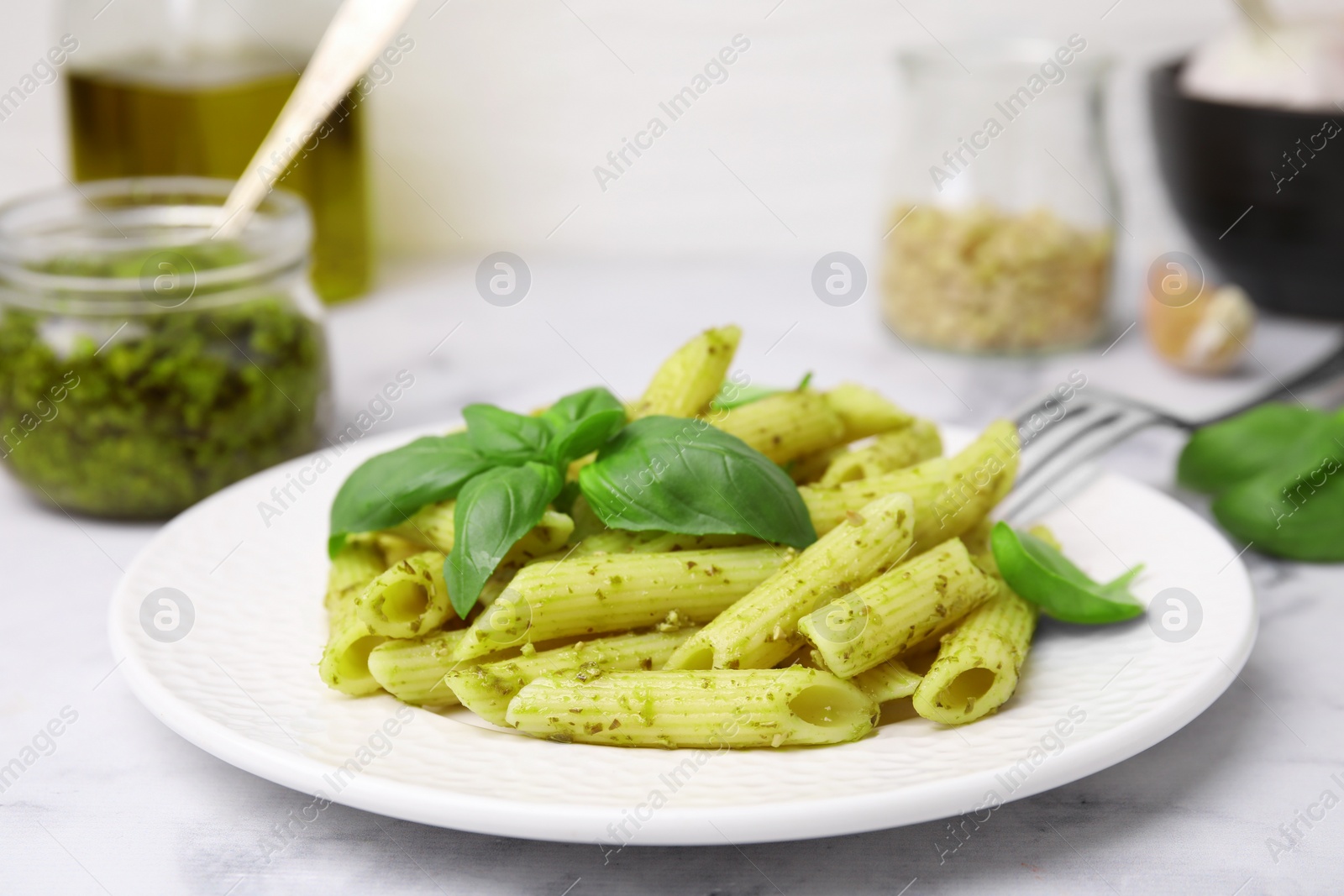 Photo of Delicious pasta with pesto sauce and basil on white marble table, closeup