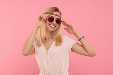 Photo of Portrait of smiling hippie woman in sunglasses on pink background