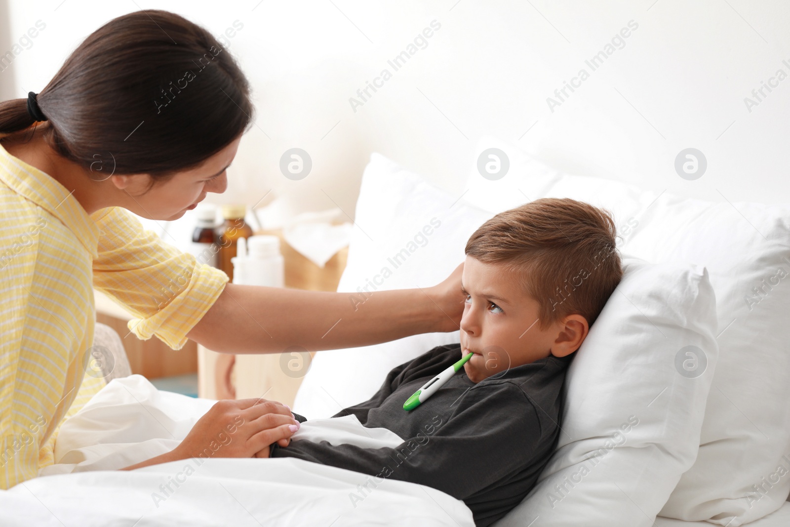 Photo of Mother measuring temperature of her sick son in bed