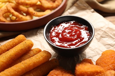 Photo of Tasty chicken nuggets, cheese sticks and ketchup on parchment paper, closeup