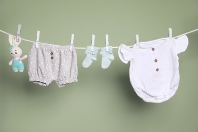Photo of Cute small baby clothes and toy hanging on washing line against green background