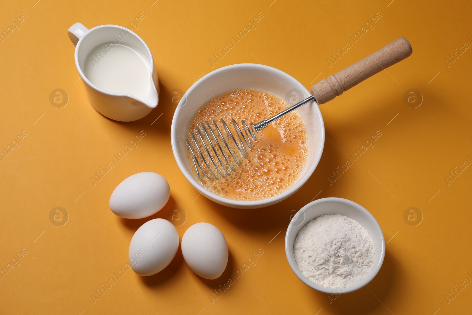 Photo of Making dough. Beaten eggs in bowl, flour and milk on orange background, above view