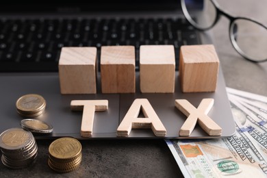 Photo of Word Tax made of wooden letters, cubes, laptop, banknotes and coins on grey table