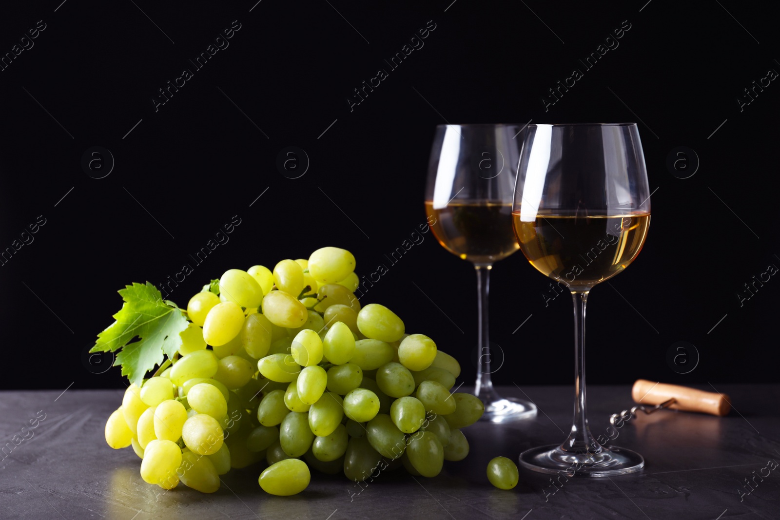 Photo of Fresh ripe juicy grapes with wineglasses on grey table against black background