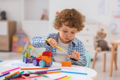 Cute little boy playing with wooden toys at white table in kindergarten